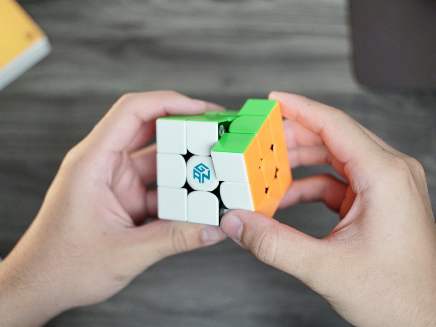 Hands solving a colorful speed cube on a wooden table.